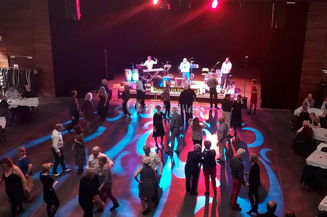 Des personnes dansent sur une piste éclairée par des lumières colorées, avec un groupe de musique jouant sur scène.