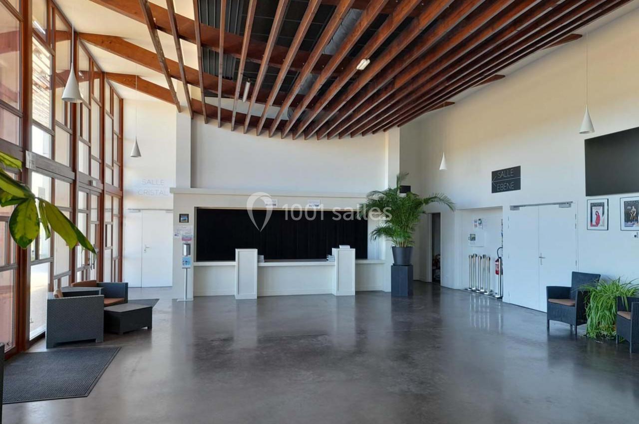 Hall lumineux avec sol en béton, plafond en bois, comptoir d'accueil, plantes et mobilier moderne.