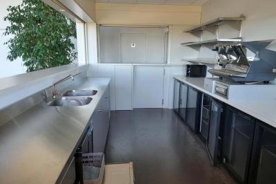 Miniature Bar Accueil avec comptoir blanc, porte-manteaux en arrière-plan, grande baie vitrée et plante verte à droite.