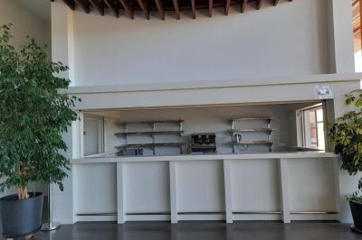 Miniature Bar Accueil avec comptoir blanc, porte-manteaux en arrière-plan, grande baie vitrée et plante verte à droite.