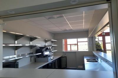 Miniature Bar Accueil avec comptoir blanc, porte-manteaux en arrière-plan, grande baie vitrée et plante verte à droite.