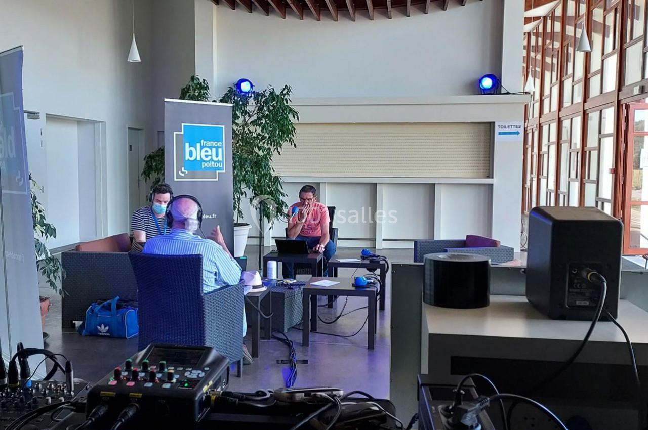 Trois personnes discutent autour d'une table équipée de matériel audio dans un espace lumineux avec des plantes.