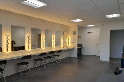 Miniature Loge Accueil avec comptoir blanc, porte-manteaux en arrière-plan, grande baie vitrée et plante verte à droite.