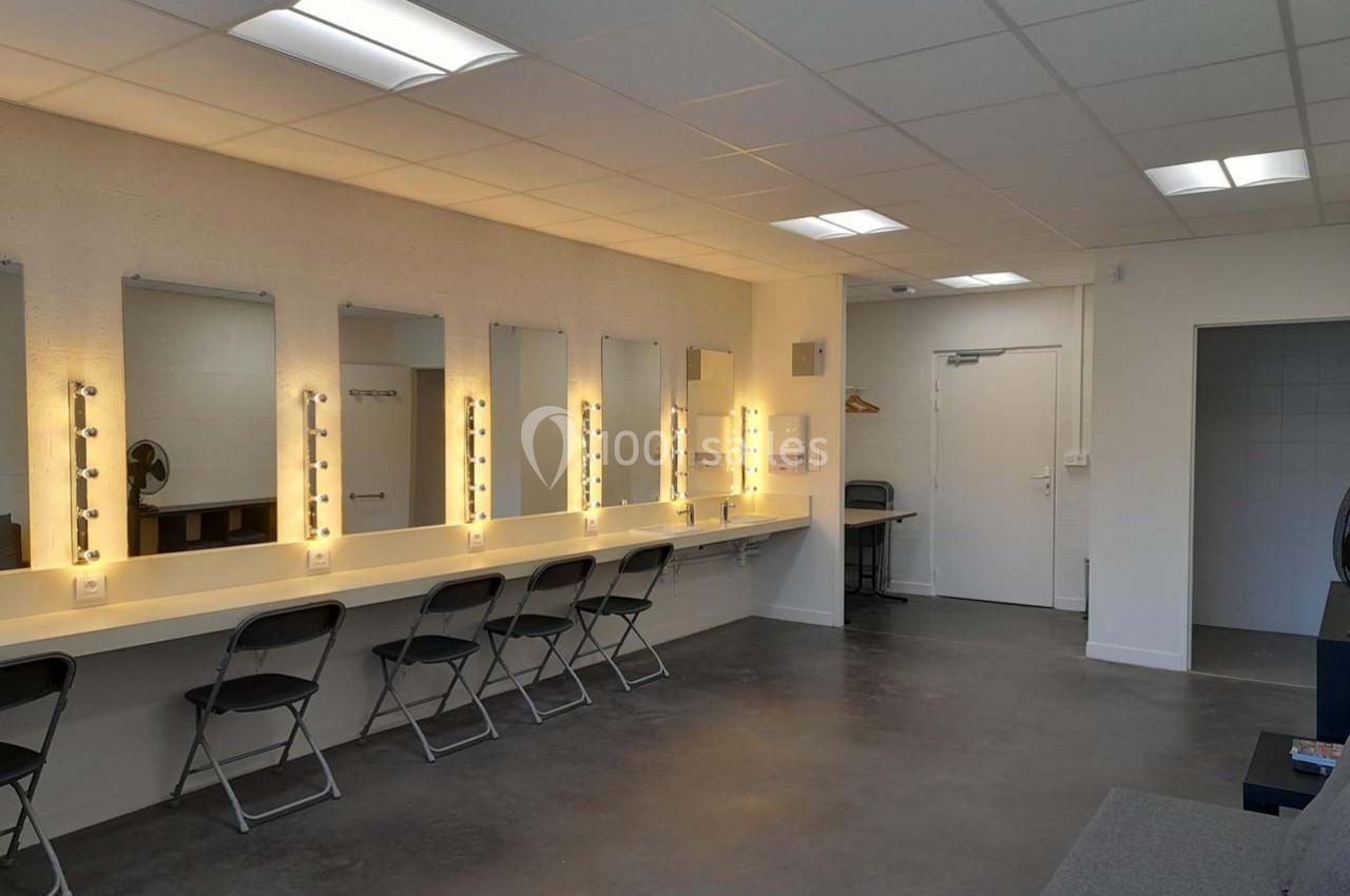 Salle de maquillage avec miroirs éclairés, tabourets pliants et murs clairs dans un espace moderne et épuré.