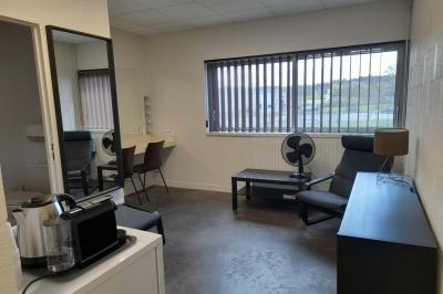 Miniature Loge Accueil avec comptoir blanc, porte-manteaux en arrière-plan, grande baie vitrée et plante verte à droite.