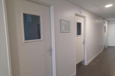 Miniature Office traiteur Accueil avec comptoir blanc, porte-manteaux en arrière-plan, grande baie vitrée et plante verte à droite.