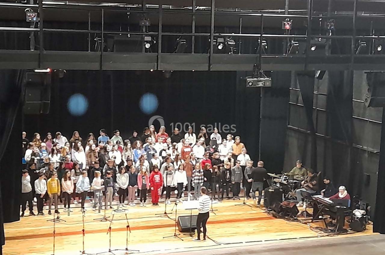Un groupe d'enfants chante sur scène, accompagné de musiciens, dans une salle de spectacle.