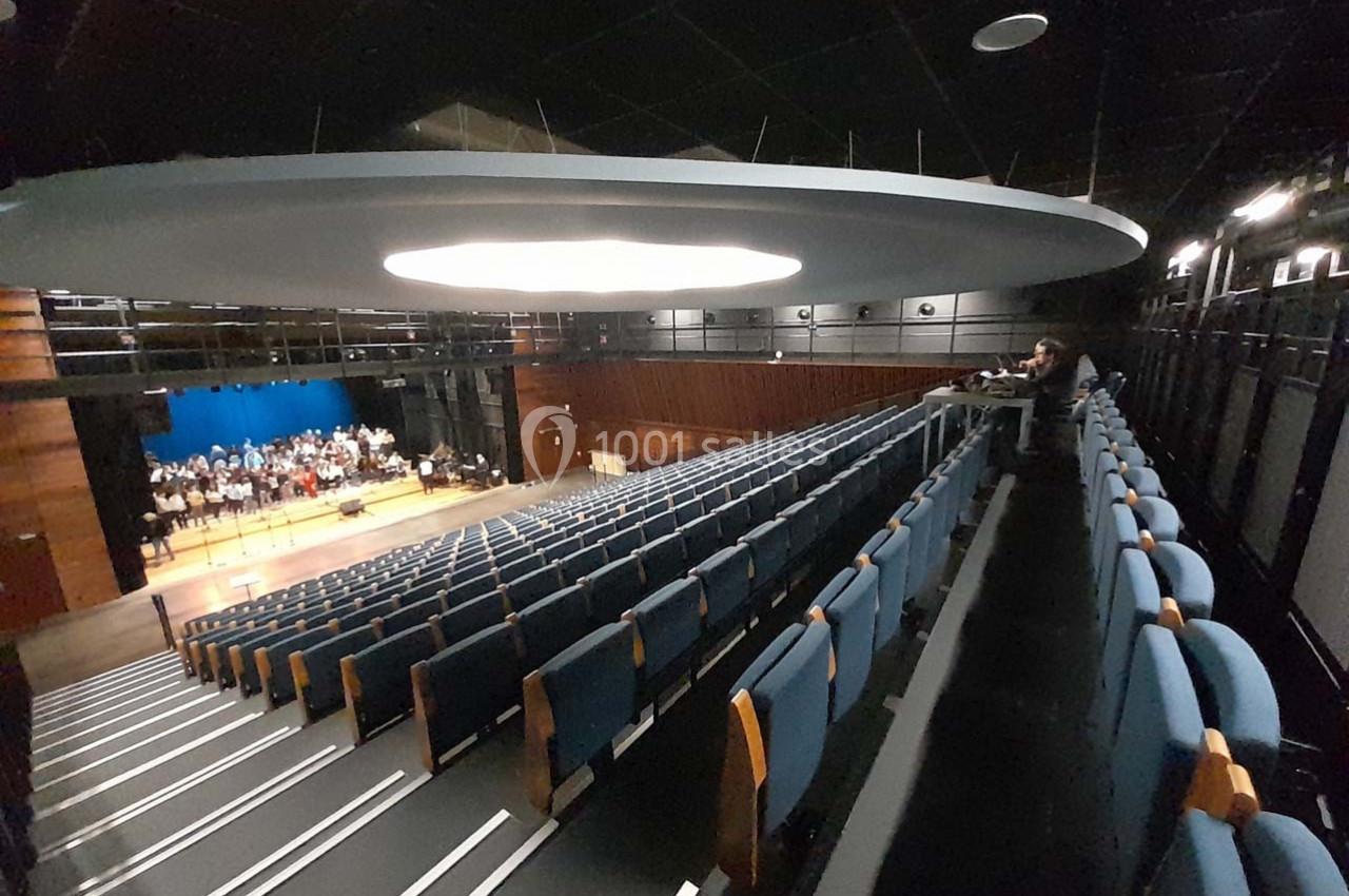 Salle de spectacle avec sièges bleus, scène éclairée en arrière-plan et quelques personnes présentes.