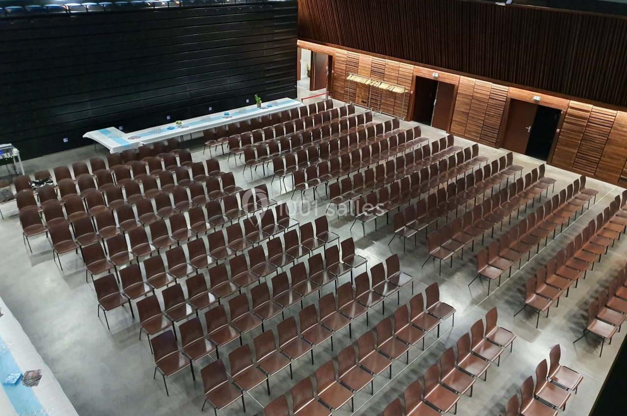 Salle de conférence vide avec des rangées de chaises marron alignées et des murs en bois sombre.