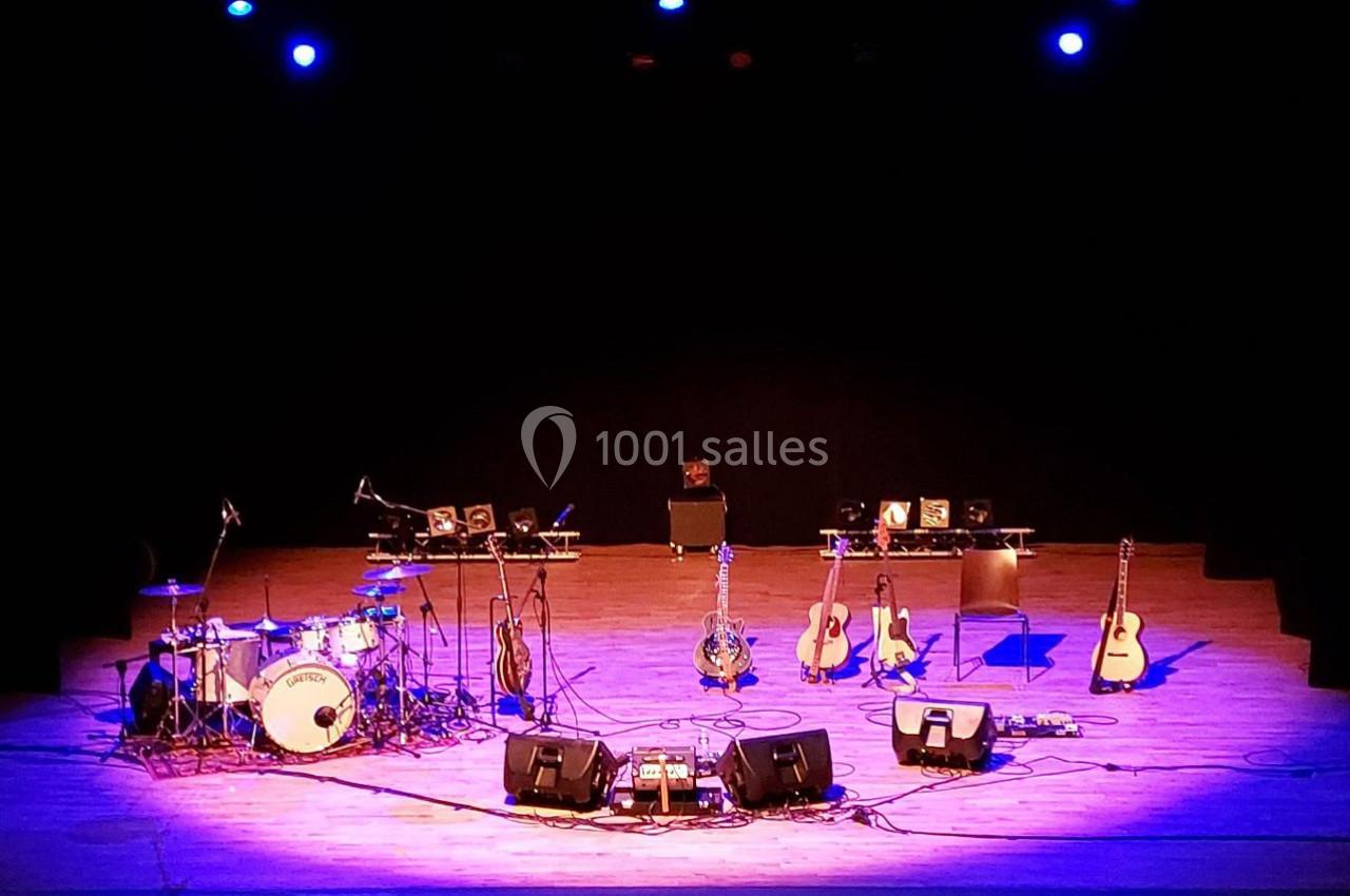 Scène de concert vide avec des instruments de musique disposés, éclairée par des projecteurs bleus.