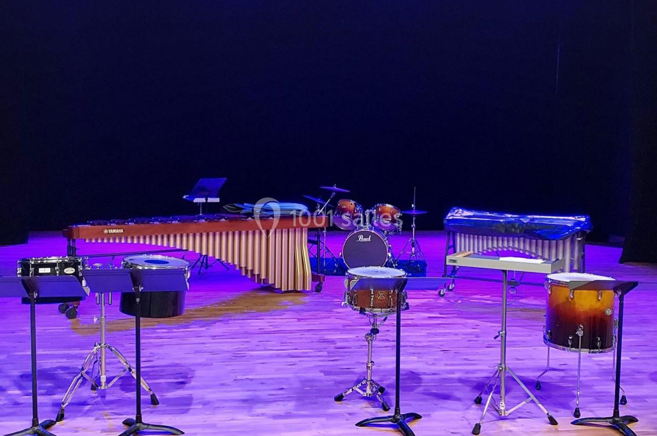 Ensemble d'instruments de percussion, incluant marimba, batterie et tambours, disposés sur une scène éclairée.