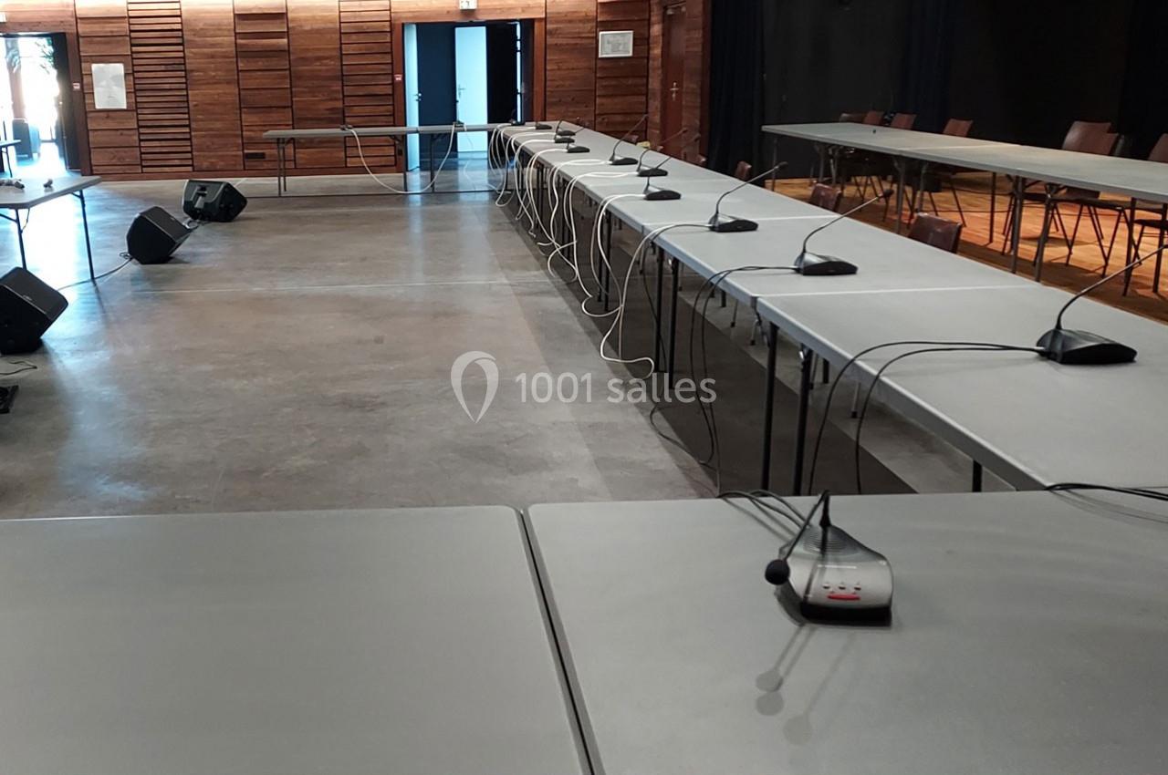 Salle de conférence avec des tables alignées, équipées de micros et câbles, dans un espace moderne en bois.