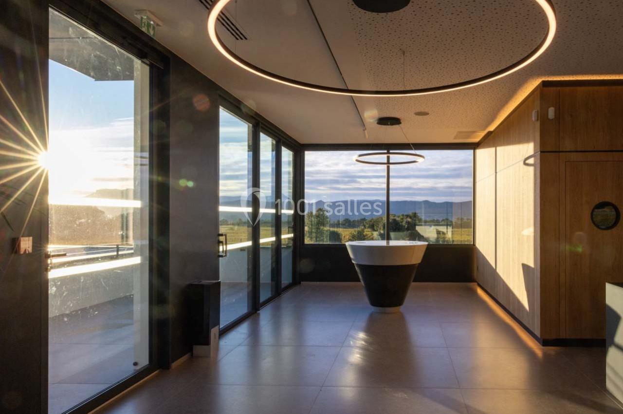 Salle lumineuse avec une grande baie vitrée, une baignoire centrale et un éclairage circulaire au plafond.