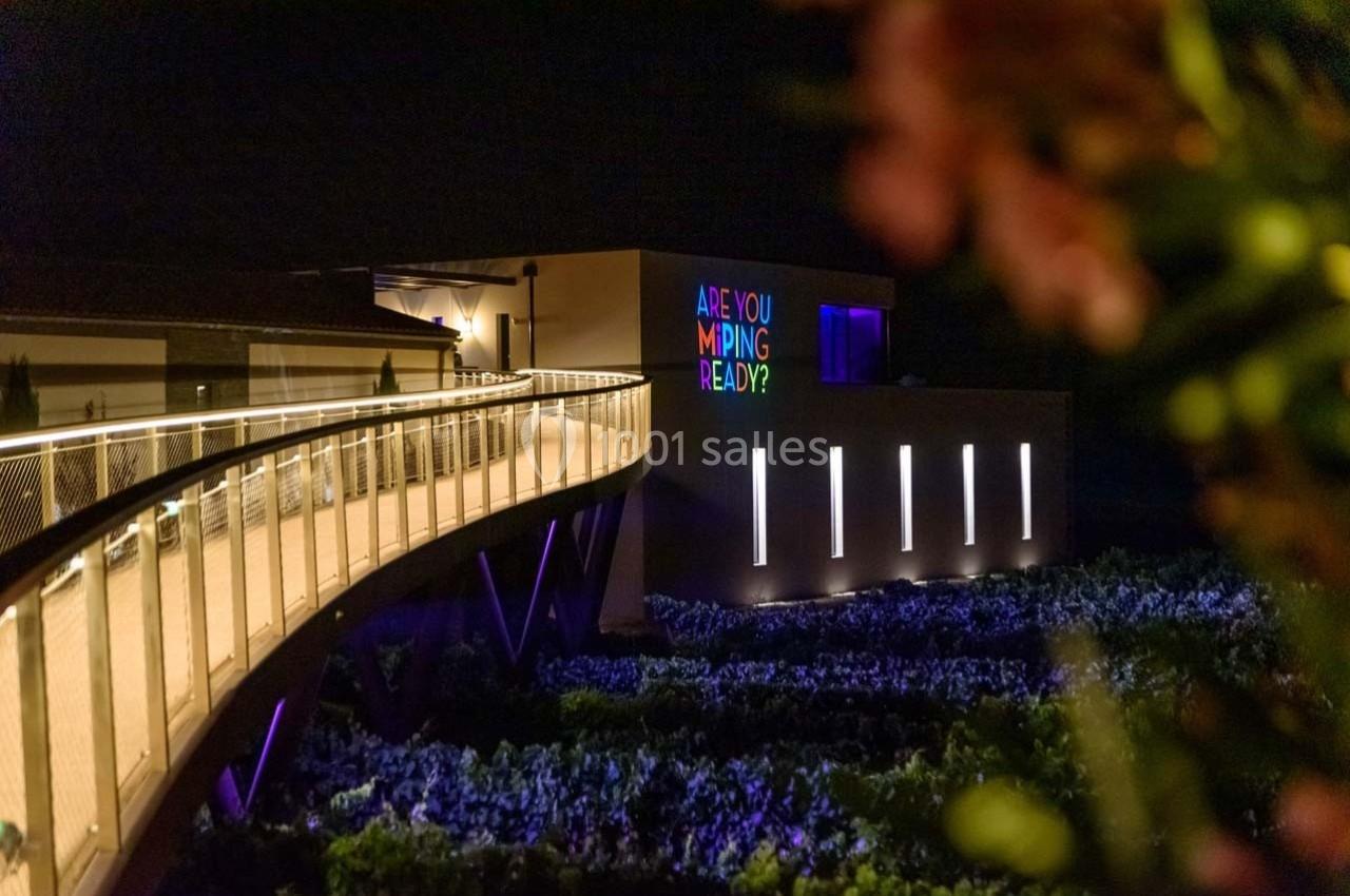 Passerelle illuminée menant à un bâtiment moderne avec une inscription lumineuse colorée, vue de nuit.