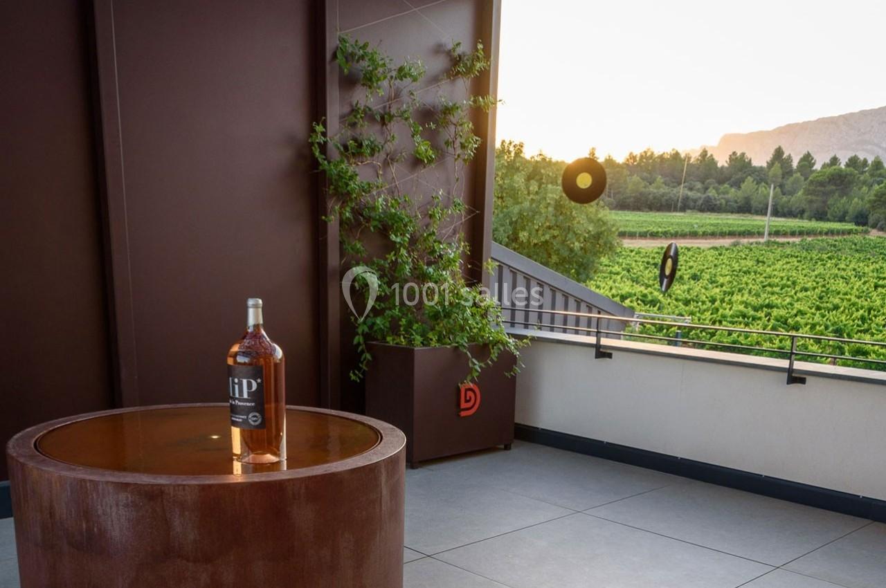 Bouteille de spiritueux posée sur une table ronde en terrasse avec vue sur un vignoble au coucher du soleil.