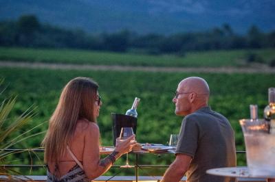 Des personnes assises à une table en extérieur, discutant et partageant un repas devant un paysage de vignobles au coucher…