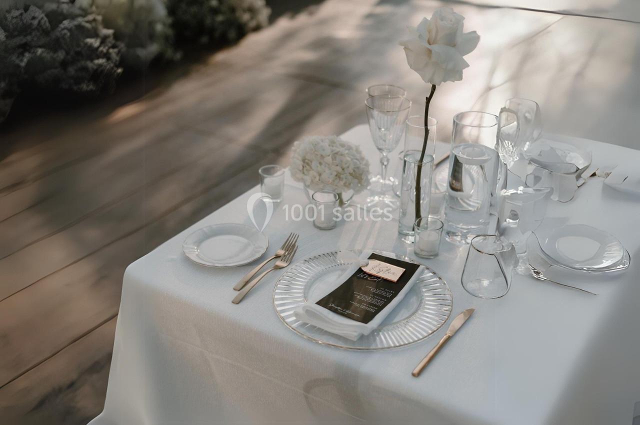 Table élégamment dressée avec nappe blanche, vaisselle raffinée, verres, couverts dorés et décoration florale.
