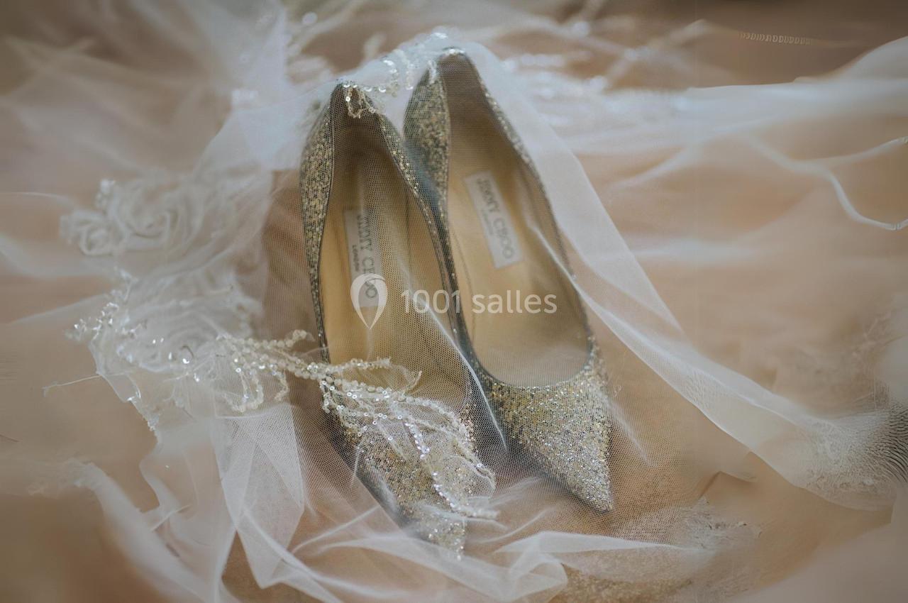 Escarpins dorés scintillants posés sur un voile en dentelle blanche.