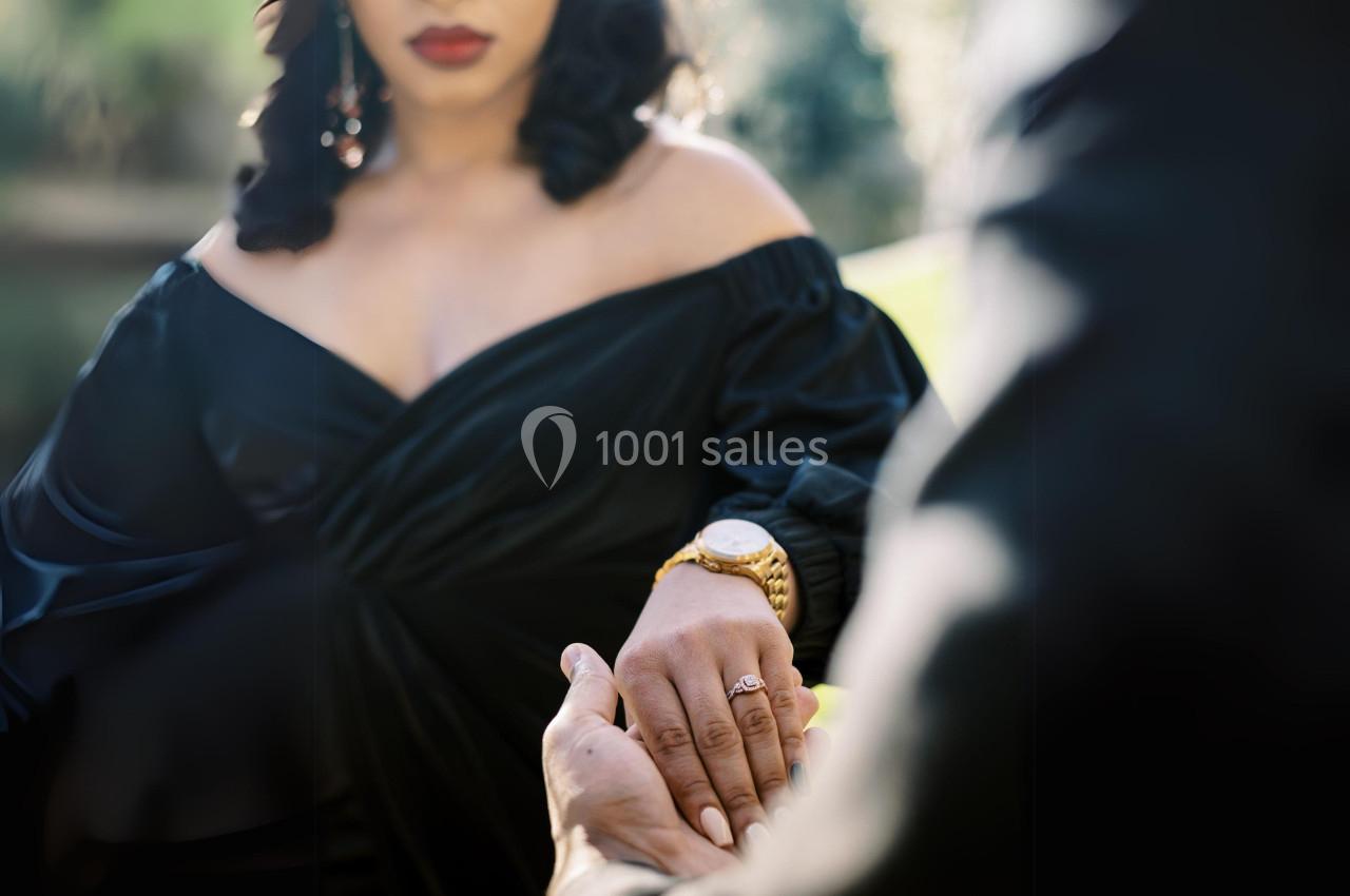 Une femme en robe noire tient la main d'une autre personne dans un cadre extérieur lumineux.