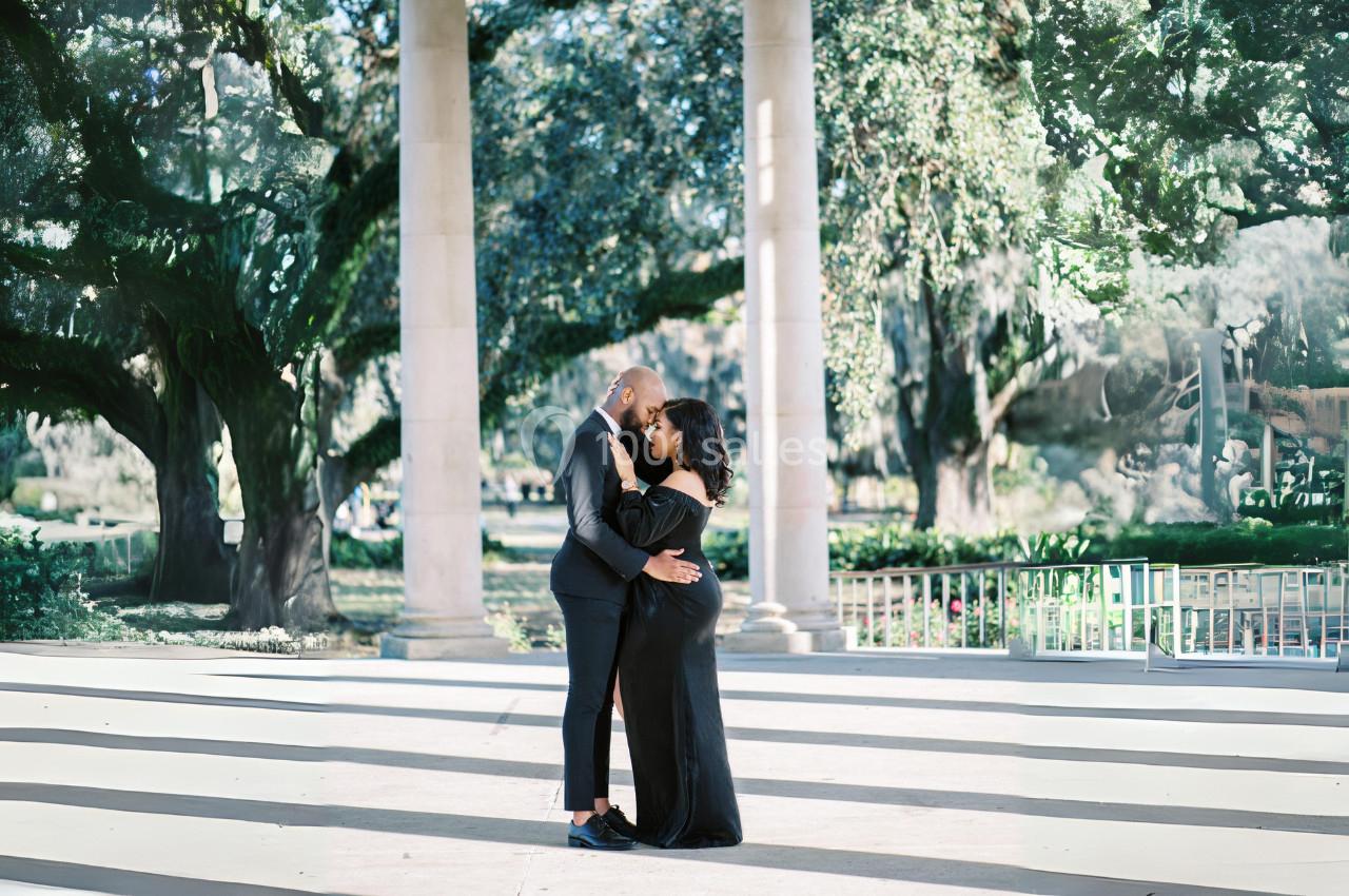 Un couple élégant s'enlace sous une pergola dans un parc verdoyant par une journée ensoleillée.