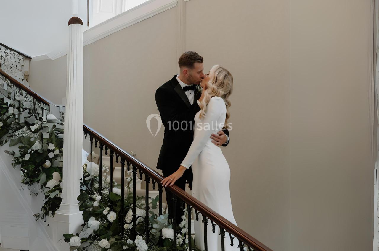 Un couple élégant s'embrasse sur un escalier décoré de fleurs blanches et de verdure.