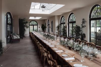 Table en bois longue dressée en extérieur, ornée de fleurs, citrons et vaisselle, entourée d'arbres et de verdure.
