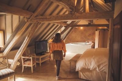 Miniature Troyes la Champagne Events #14 Femme de dos dans une chambre mansardée avec poutres apparentes, lit, télévision et baignoire en arrière-plan.