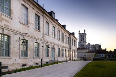 Miniature Troyes la Champagne Events #3 Femme de dos dans une chambre mansardée avec poutres apparentes, lit, télévision et baignoire en arrière-plan.