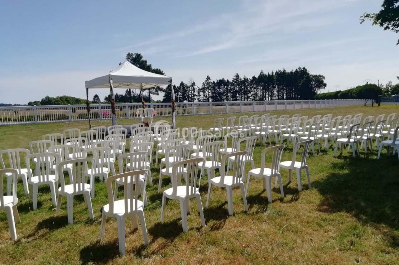 Chaises blanches disposées en rangées sur une pelouse, face à une tente blanche sous un ciel dégagé.
