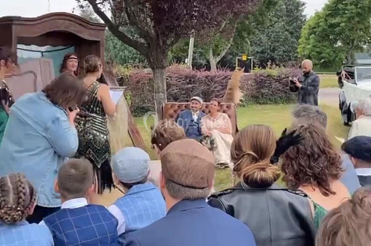 Un couple assis lors d'une cérémonie en plein air, entouré d'invités et d'un décor champêtre.