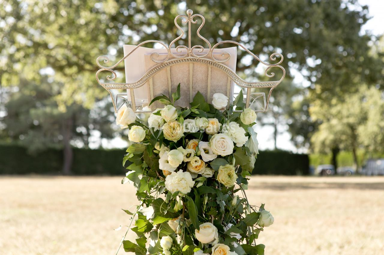 Arrangement floral avec des roses blanches et jaunes décorant un support métallique dans un cadre extérieur verdoyant.