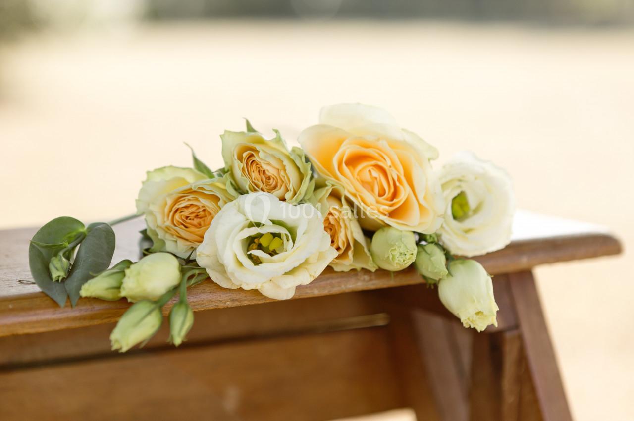 Bouquet de fleurs jaunes et blanches posé sur un banc en bois, avec un arrière-plan flou extérieur.