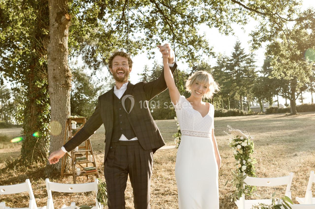 Un couple souriant en tenue de mariage marche main dans la main dans un cadre extérieur ensoleillé.