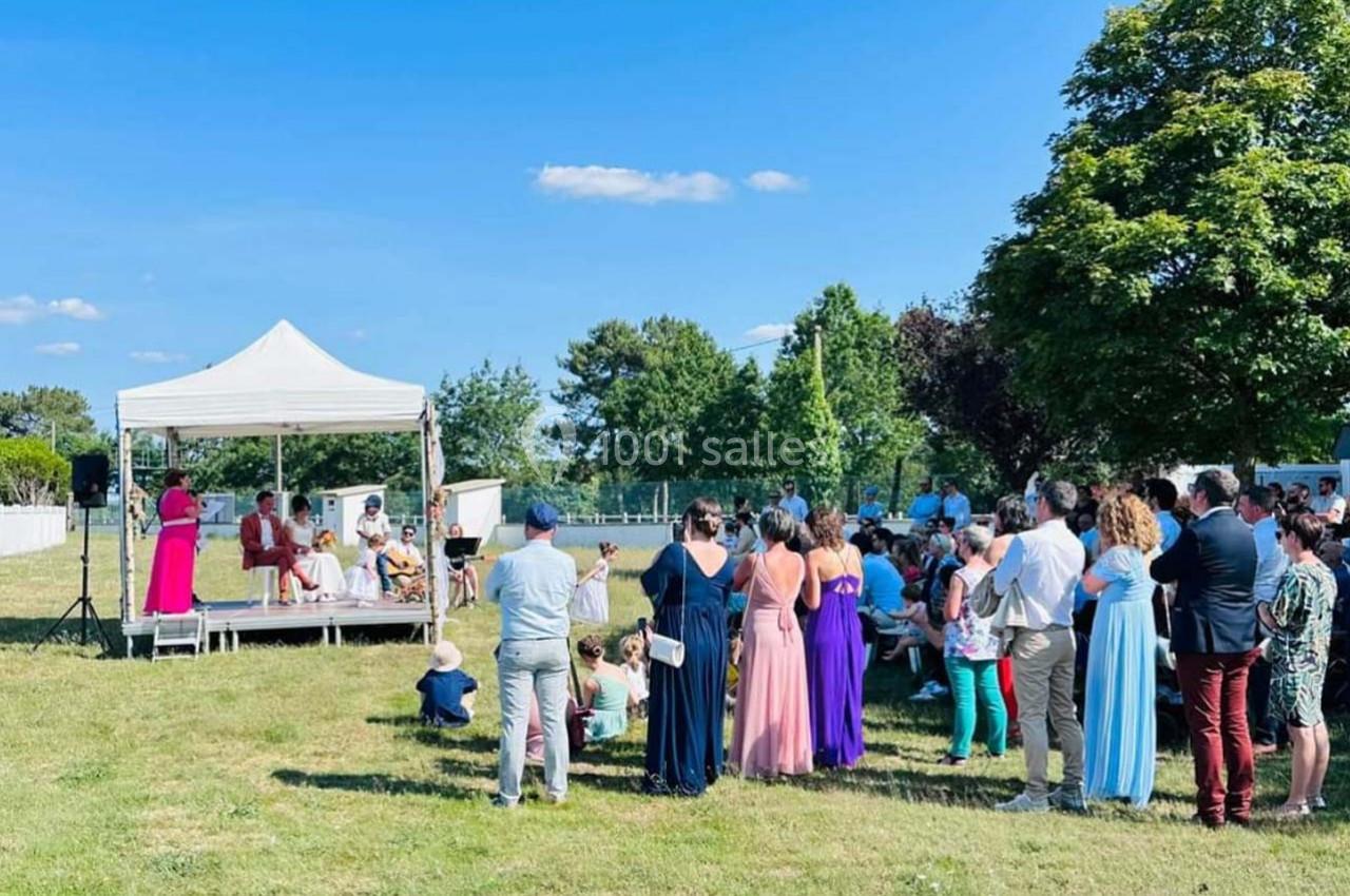 Groupe de personnes rassemblées en plein air autour d'une scène sous une tente blanche lors d'un événement.