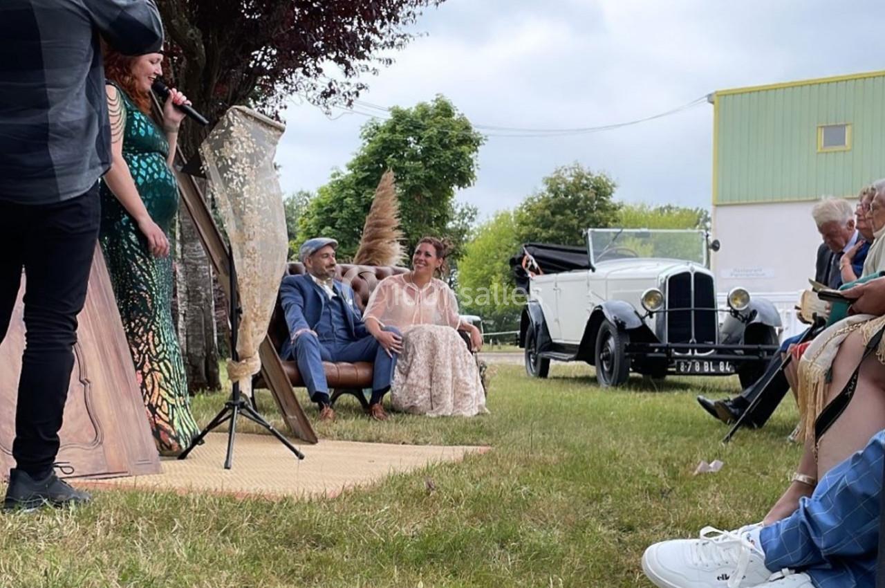 Un couple assis sur un canapé en extérieur lors d'une cérémonie, avec une voiture ancienne en arrière-plan.