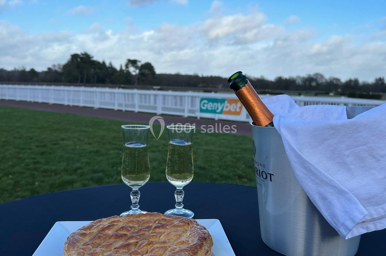Une galette sur une assiette, deux verres de champagne et un seau avec une bouteille, en extérieur près d'un champ.