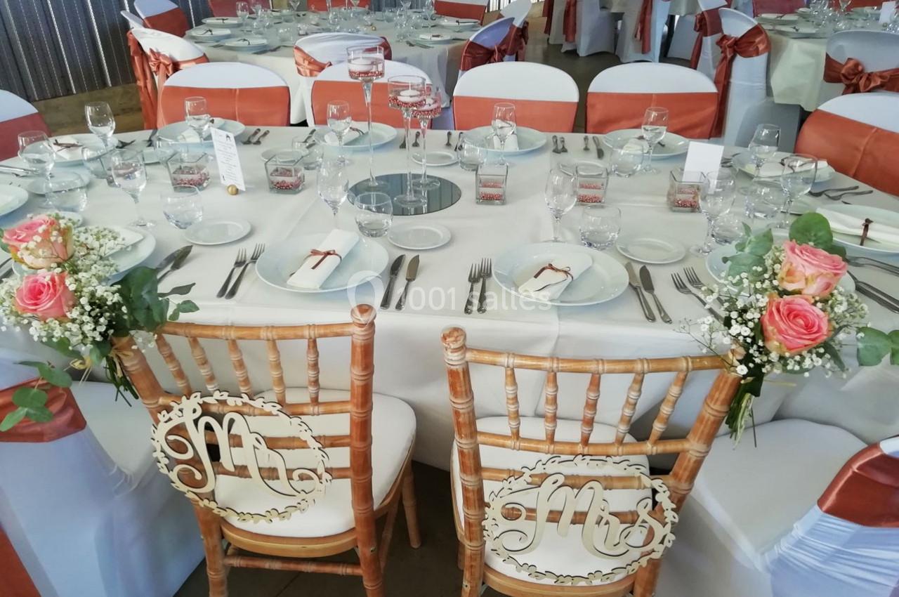 Chaises décorées pour les mariés devant une table de réception élégamment dressée avec vaisselle et fleurs.