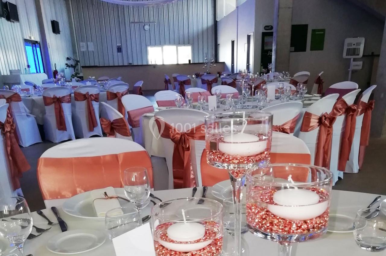 Salle de réception décorée avec des tables dressées, chaises ornées de nœuds rouges et bougies flottantes en centre de table.