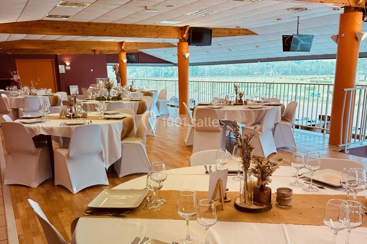 Salle de réception lumineuse avec tables rondes dressées, nappes blanches et décorations naturelles en bois et fleurs…