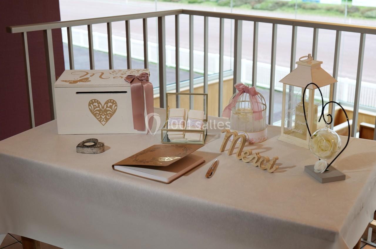 Table décorée pour un mariage avec urne, livre d'or, bougie, rubans roses et éléments en bois doré.