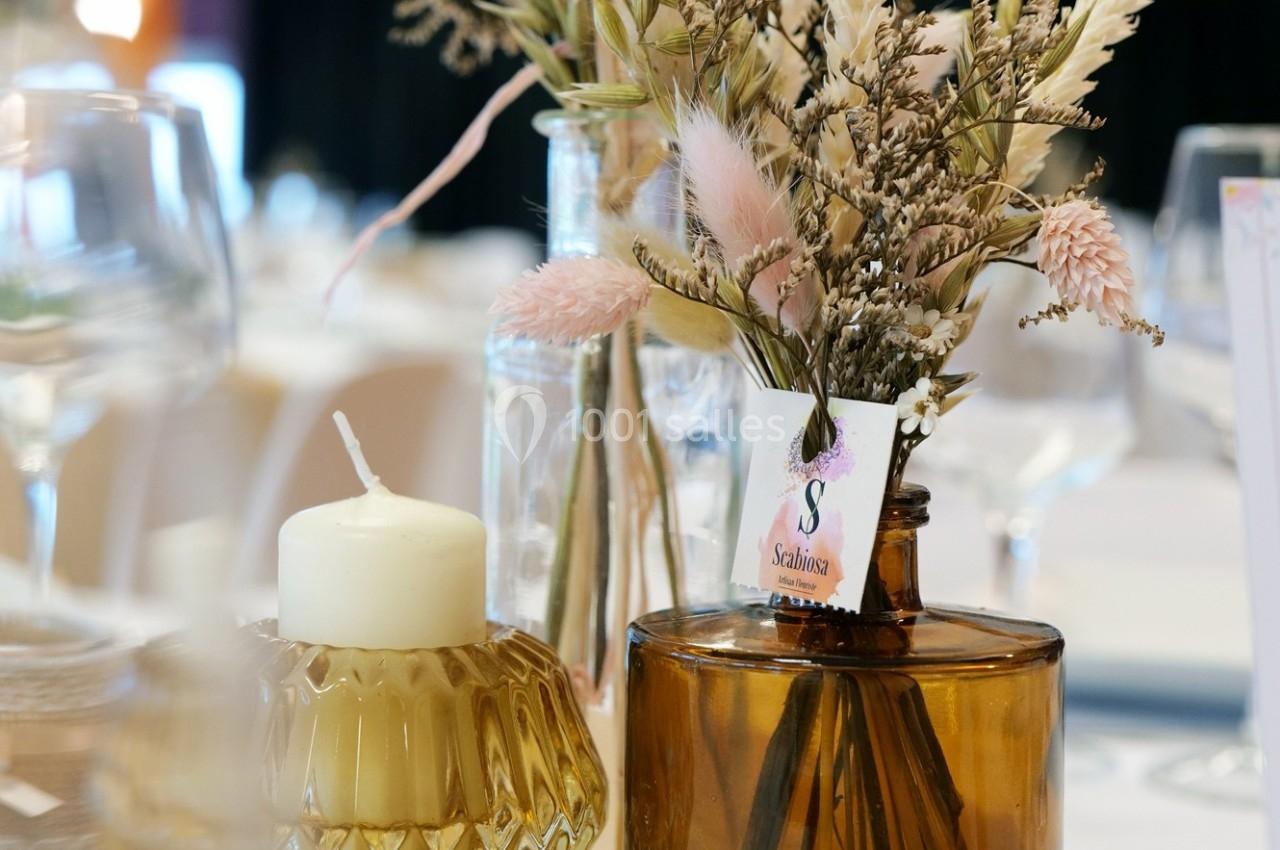 Bouquet de fleurs séchées dans un vase ambré, accompagné d'une bougie blanche sur une table décorée.