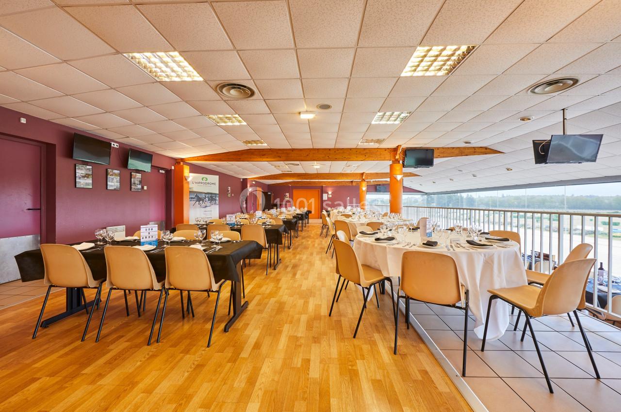Salle de réception lumineuse avec tables dressées pour un repas, chaises en bois et vue sur l'extérieur par de grandes baies…