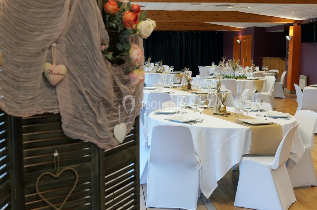 Salle de réception décorée avec des tables rondes dressées, nappes blanches et détails floraux élégants.