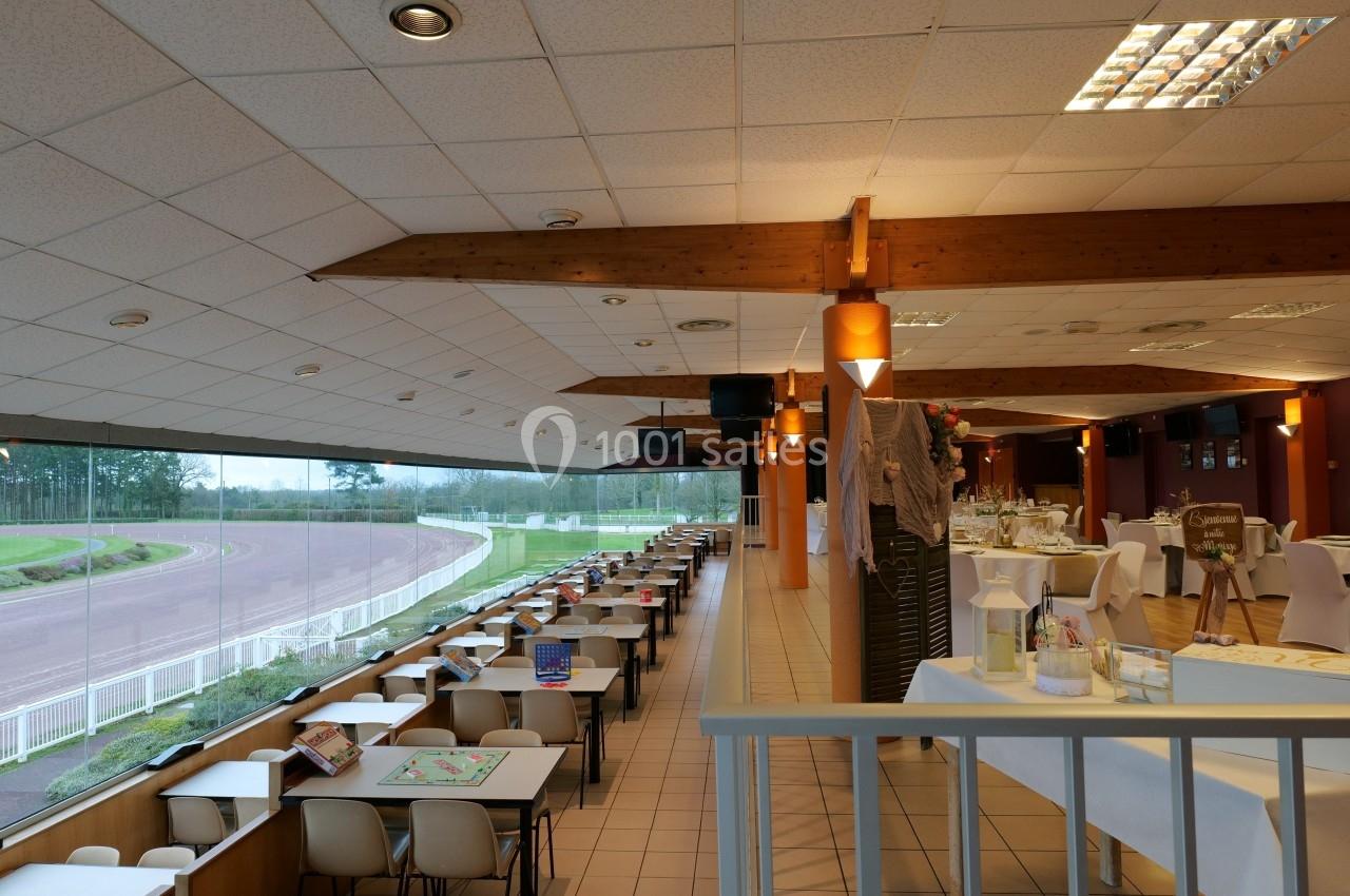 Salle de restaurant avec vue sur un hippodrome, tables dressées à gauche et espace événementiel à droite.