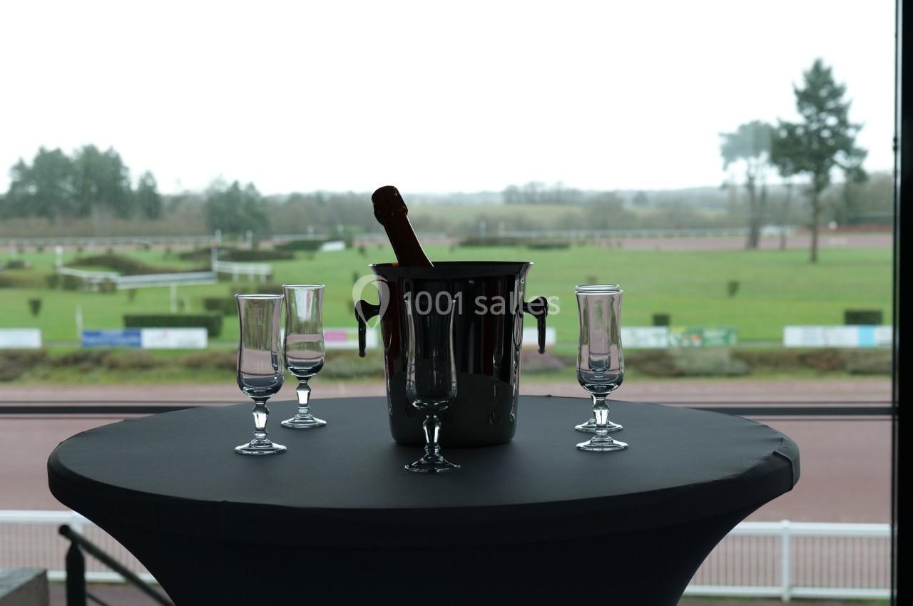 Seau à champagne avec bouteille et quatre flûtes vides sur une table, vue sur un paysage extérieur avec pelouse.