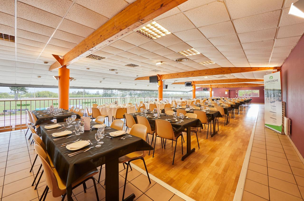 Salle de réception lumineuse avec tables dressées, nappes noires, chaises beige et vue sur l'extérieur.