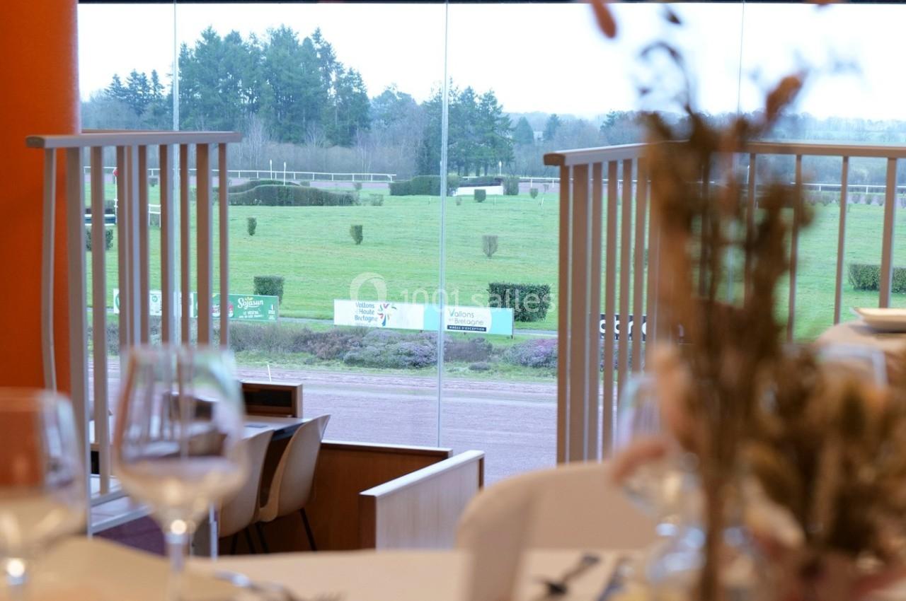 Vue sur un champ verdoyant et une piste extérieure depuis une salle avec des tables dressées.