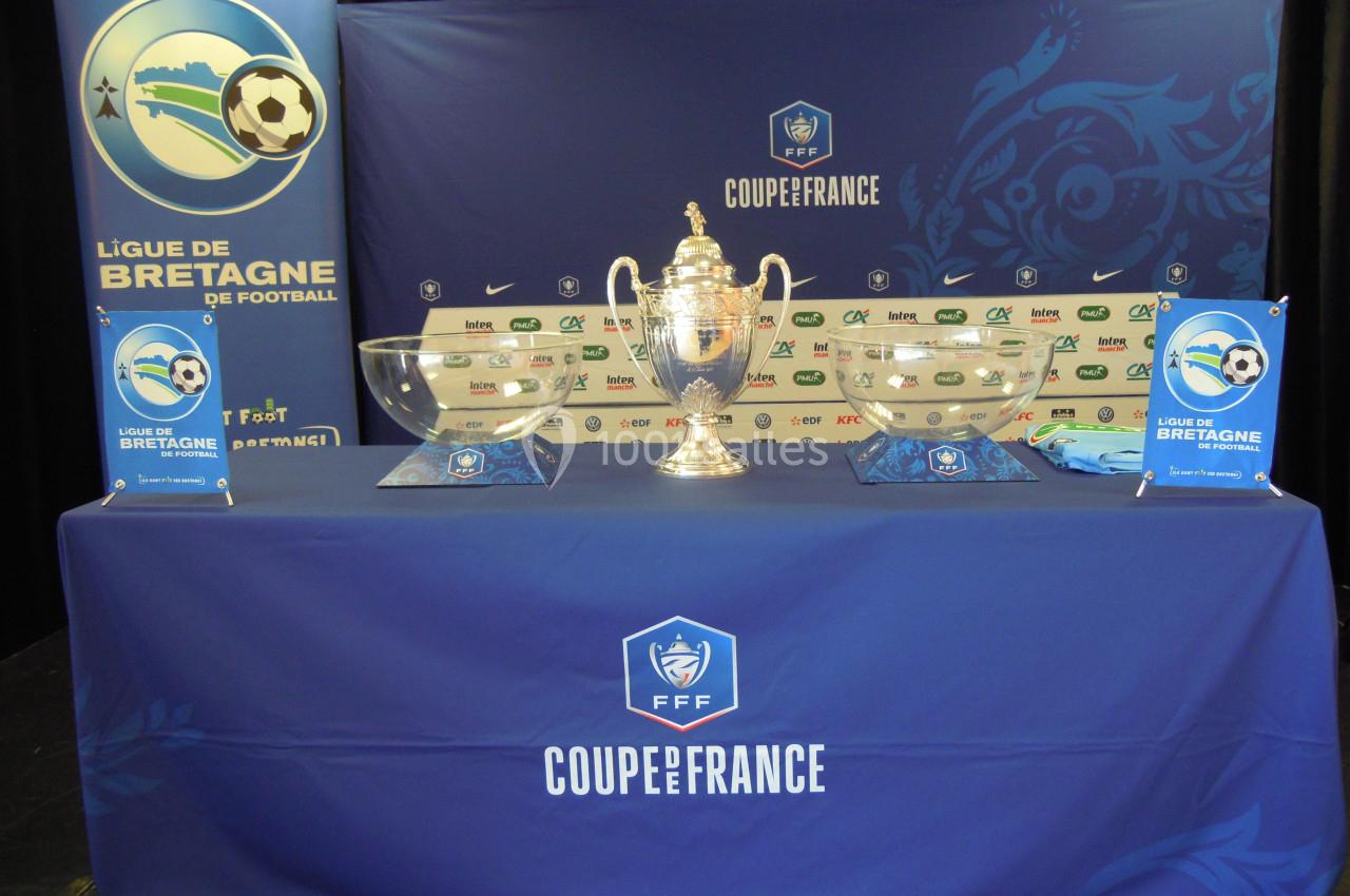 Trophée de la Coupe de France exposé sur une table ornée de logos de la Ligue de Bretagne et de sponsors.
