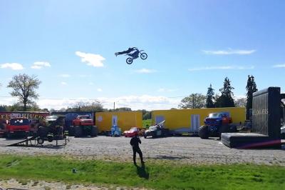 Un motocycliste effectue un saut spectaculaire au-dessus de véhicules dans un espace extérieur ensoleillé.