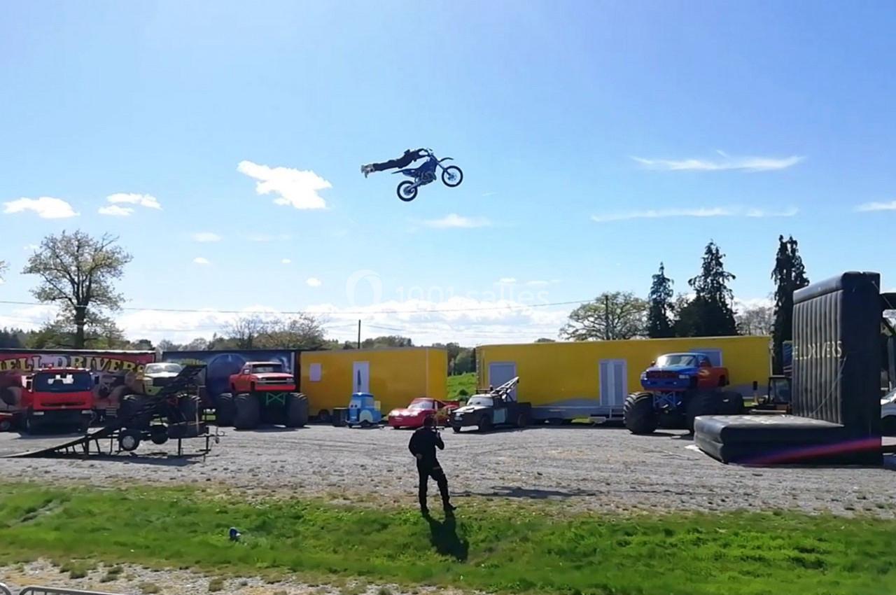 Un motocycliste effectue un saut spectaculaire au-dessus de véhicules dans un espace extérieur ensoleillé.